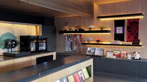 A reception area with a wooden counter, two black refrigerators, traditional Japanese artwork, and a shelf with various items including a framed certificate. - Tokyu Stay Kyoto Sakaiza Shijo-Kawaramachi (Kyoto)