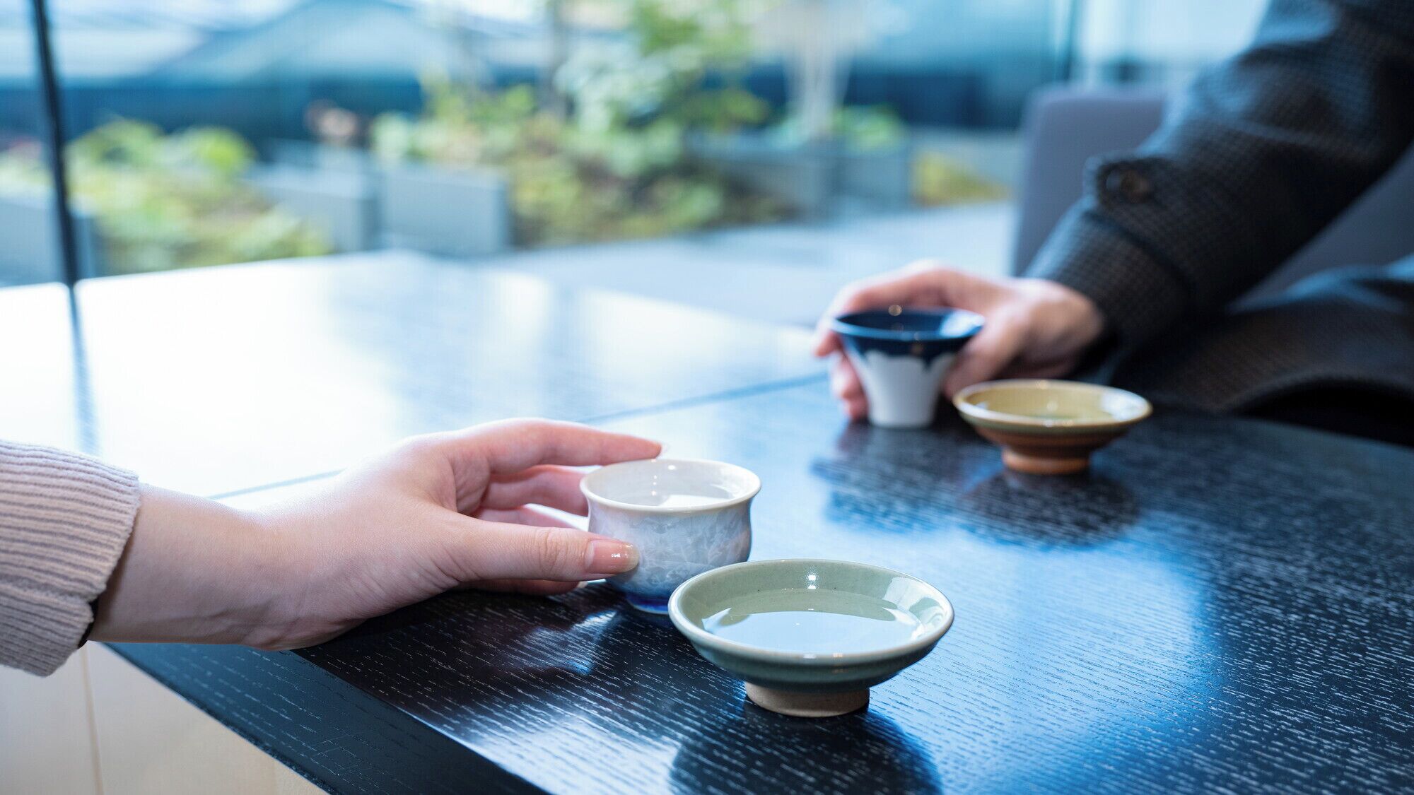 A table with three ceramic cups and saucers, a hand holding a cup, and a person in the background.