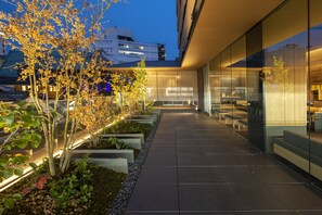 Un bâtiment moderne doté d’une façade en verre, d’un espace extérieur aménagé pour s’asseoir et d’un jardin paysager bien entretenu.