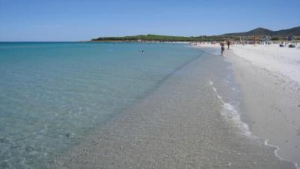 Une plage à l’eau claire, un rivage sablonneux et une colline qui se dessine à l’horizon.