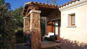 Un espace extérieur abrité, doté de piliers en pierre, d’une terrasse et d’un bâtiment avec une fenêtre et une porte.