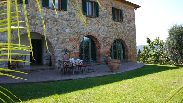 Ein Steinhaus mit Bogenfenstern und einer Terrasse mit Außenplätzen.