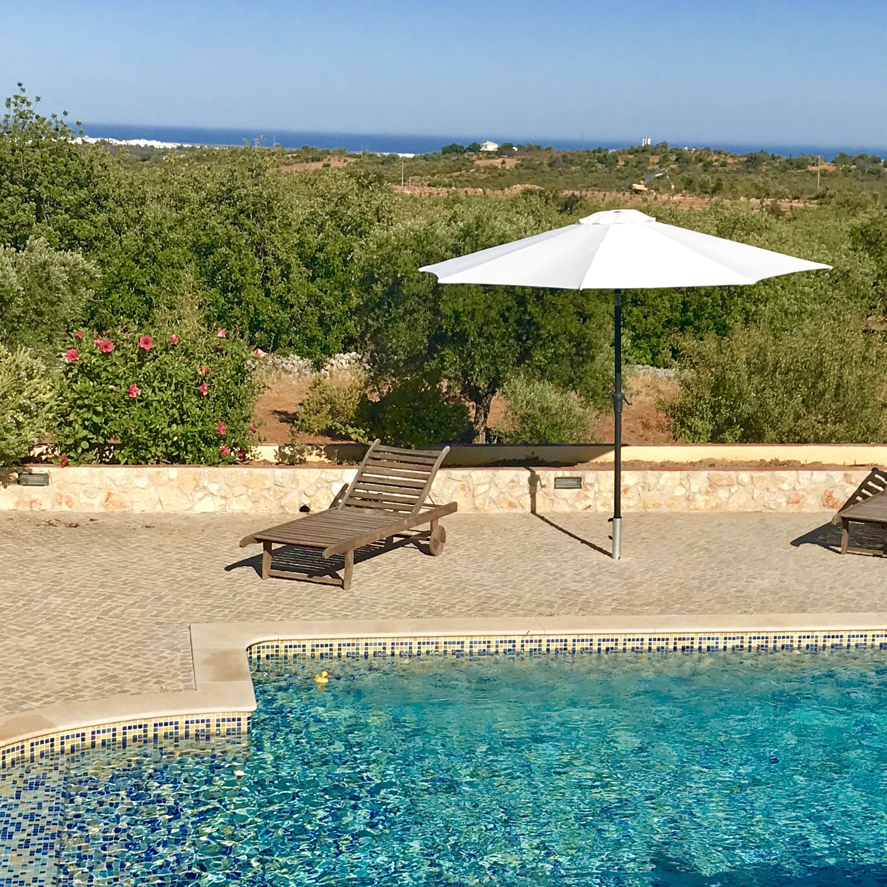 Un espace piscine offrant une vue dégagée sur l’océan, une chaise longue et un parasol blanc.