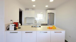 Une cuisine moderne avec des meubles blancs, un réfrigérateur en acier inoxydable et un plan de travail sur lequel se trouvent un extracteur de jus et des oranges.