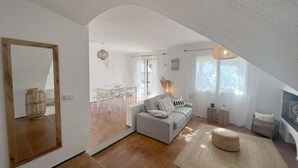 Un vaste espace de vie doté d’un haut plafond, d’une table à manger avec des chaises, d’un canapé gris et d’un grand miroir.