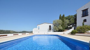 Une piscine d’un bleu éclatant, avec un bâtiment blanc en arrière-plan et une vue sur des collines.
