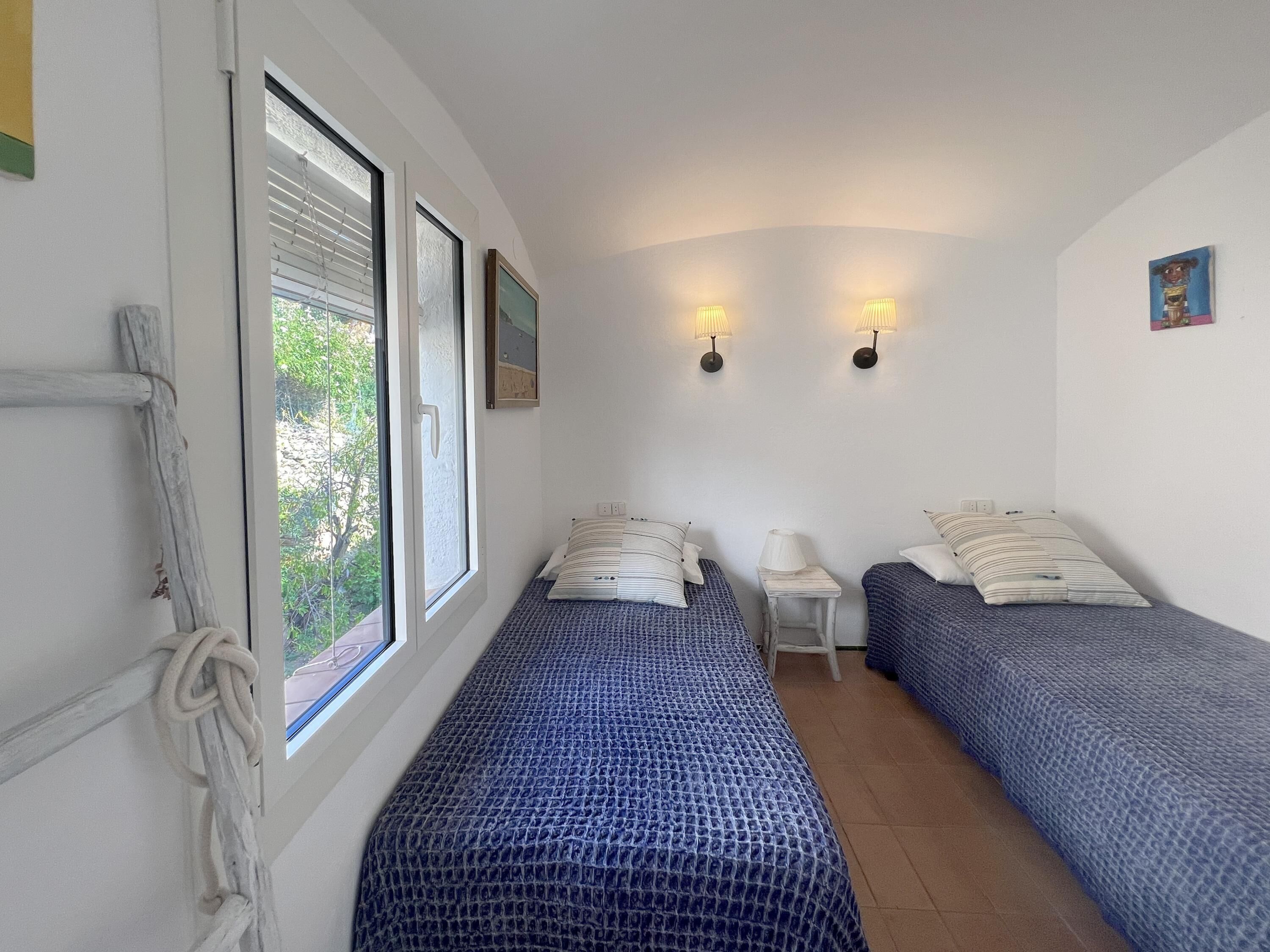 A room with two beds, a small table, and a window with blinds.
