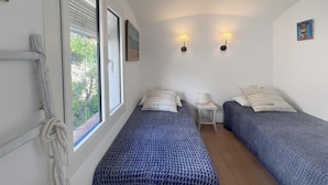 Une chambre avec deux lits, une petite table et une fenêtre avec des stores.