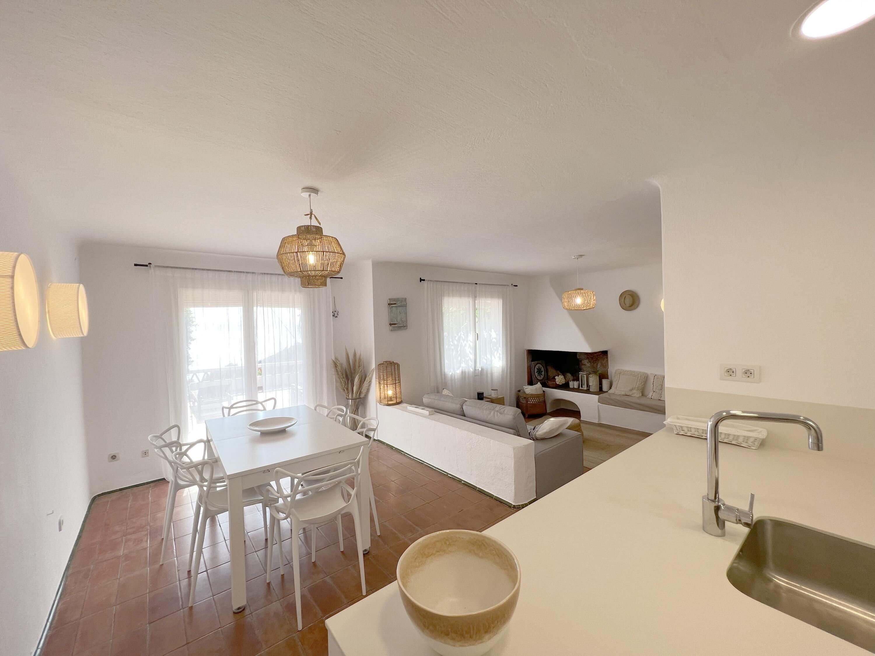 A modern kitchen with white cabinetry, a dining area with a white table and chairs, and a living area with a sofa and a coffee table.