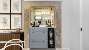A bar area with a mirror, wine glasses, and bottles. There are framed pictures on the wall and a white chair. - New! Everything BRAND new 23-  Luxury Prime Location Great for Family & Friends (Lisboa)