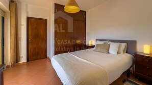 Una habitación de hotel con una cama, un armario de madera, una puerta, una lámpara de techo y una mesita de noche con lámpara.