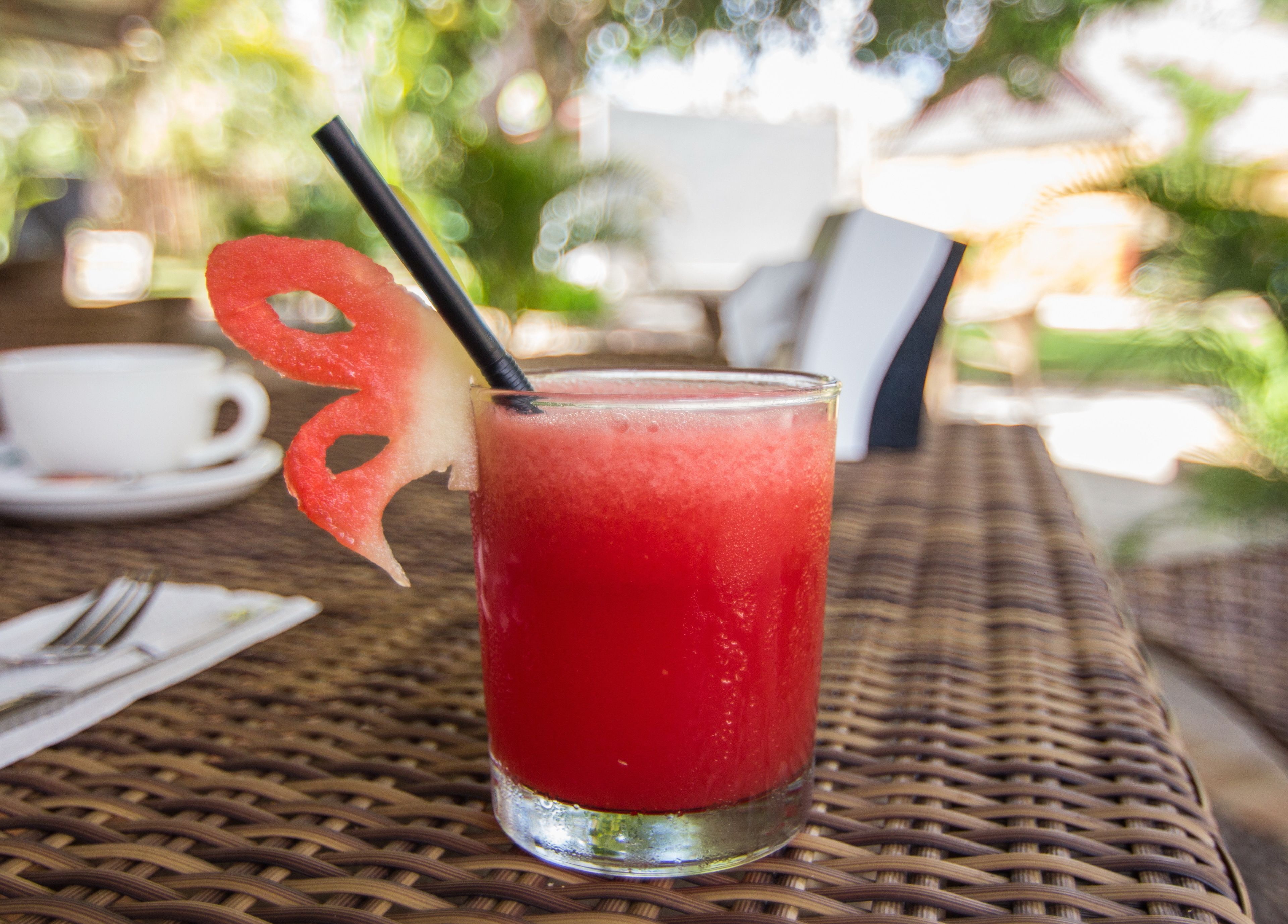 A glass of red beverage with a black straw and a decorative fruit slice on a wicker table.