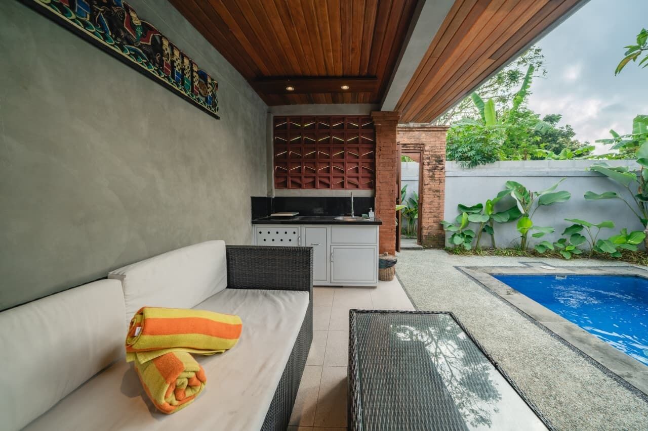 A covered outdoor area with a sofa, a small kitchen, and a swimming pool.
