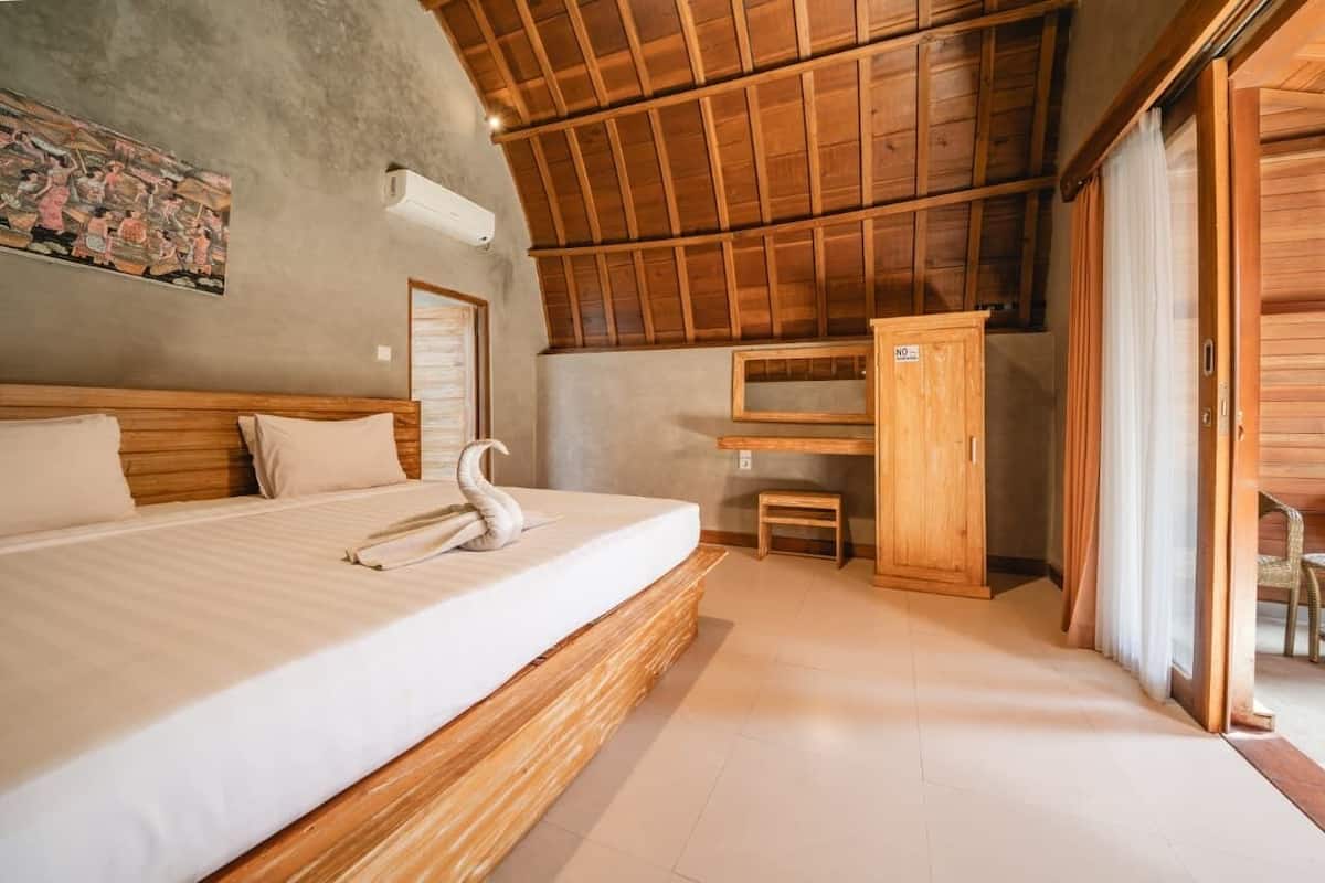 Une chambre avec un lit en bois, une petite armoire en bois et une grande fenêtre.