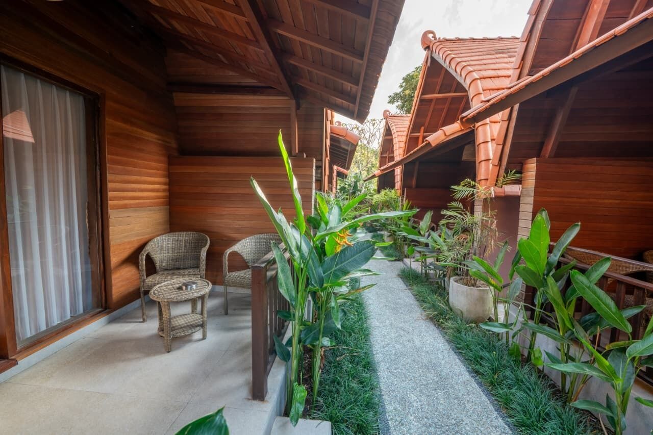 A wooden corridor with a pathway, wicker chairs, and potted plants.