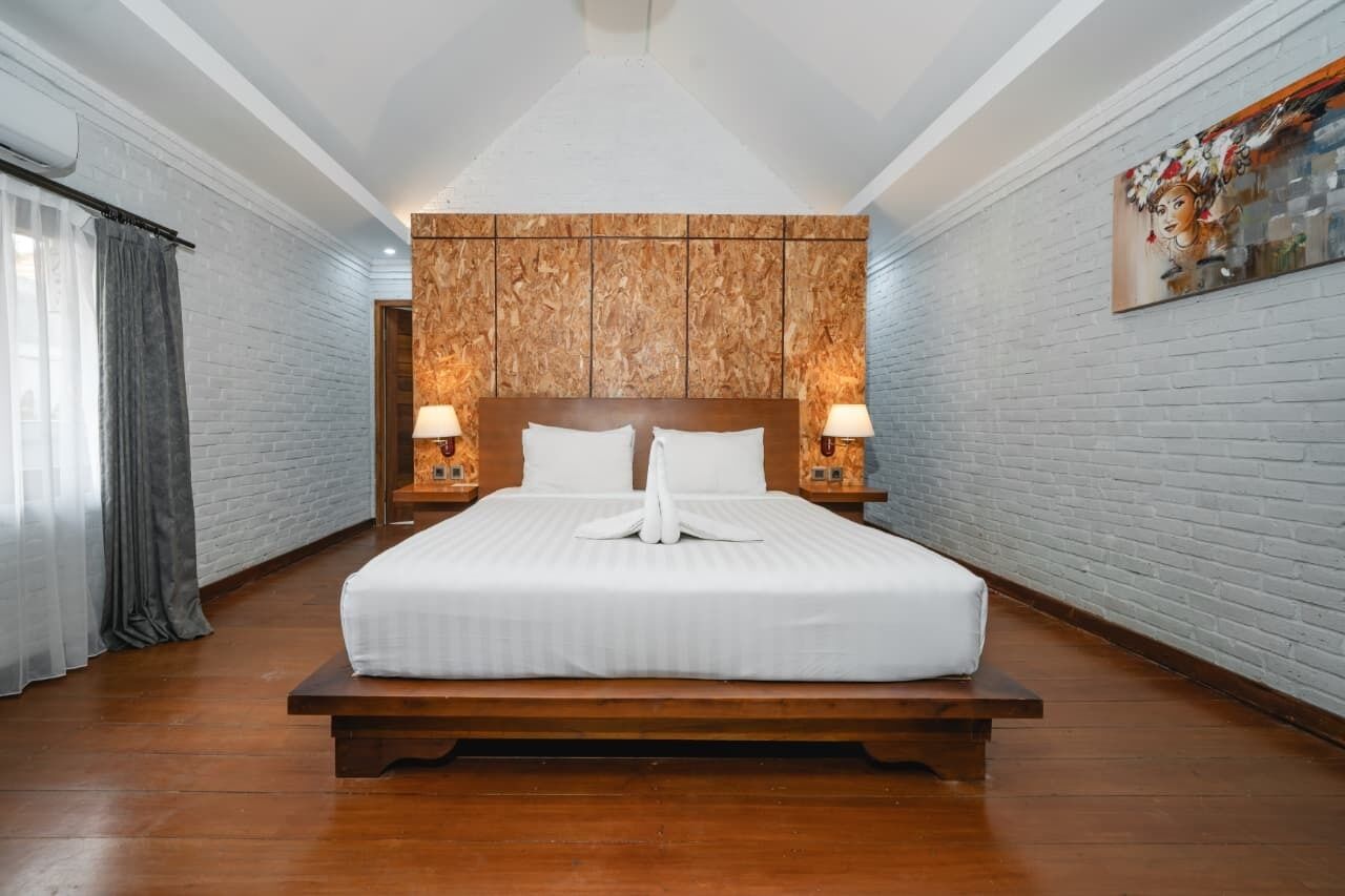 A large bed with a wooden headboard, two bedside lamps, and a decorative towel arrangement.
