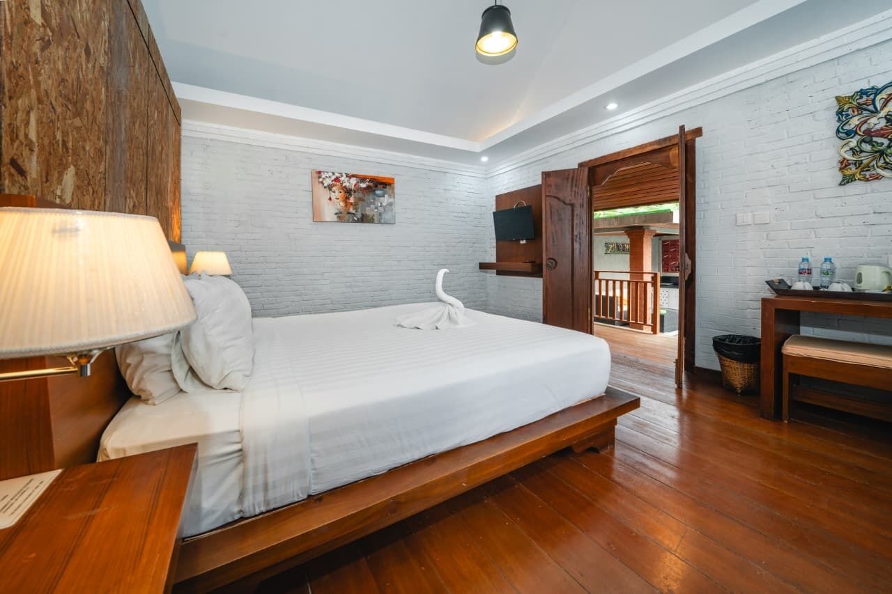 A hotel room with a wooden bed, a desk with a chair, a TV mounted on the wall, and a wooden door leading to a balcony.