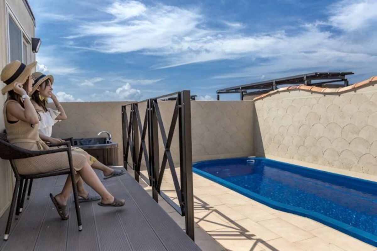Un área junto a la piscina con sillas de descanso y una mesa.