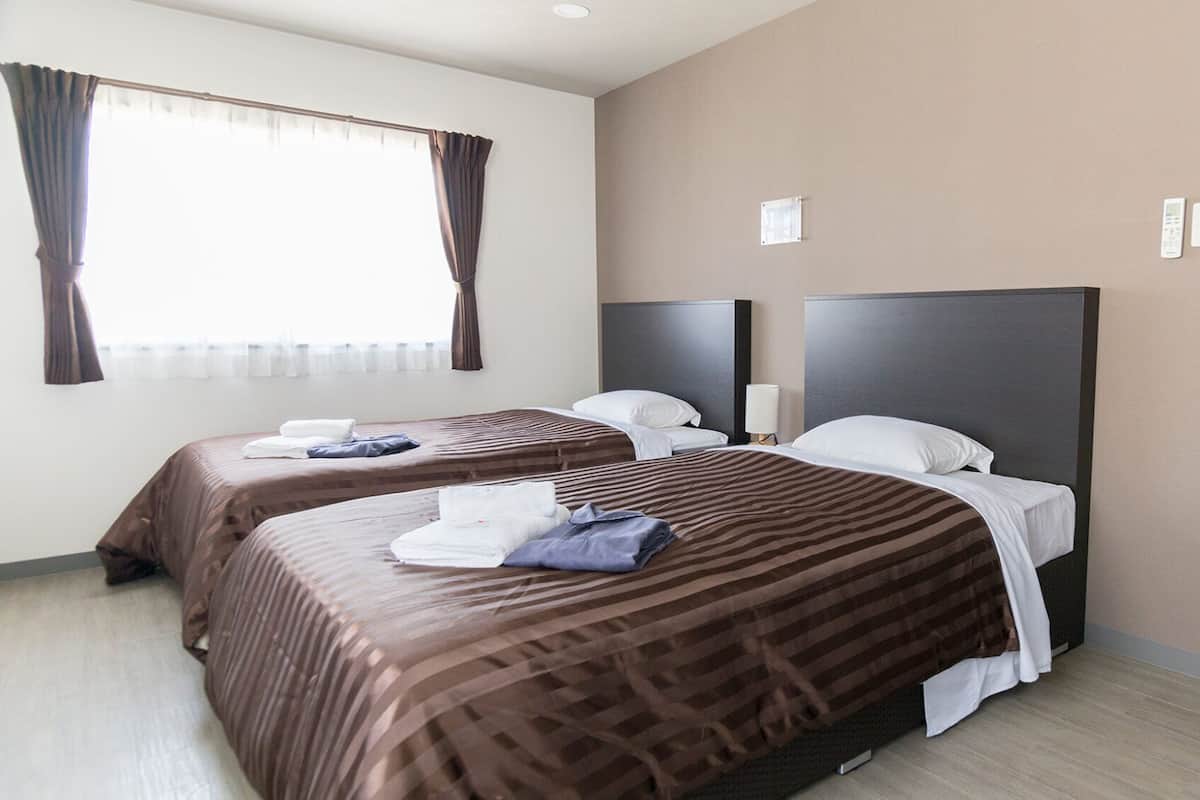 Une chambre d’hôtel avec deux lits, une fenêtre avec des rideaux, une table de chevet et une porte avec une poignée.