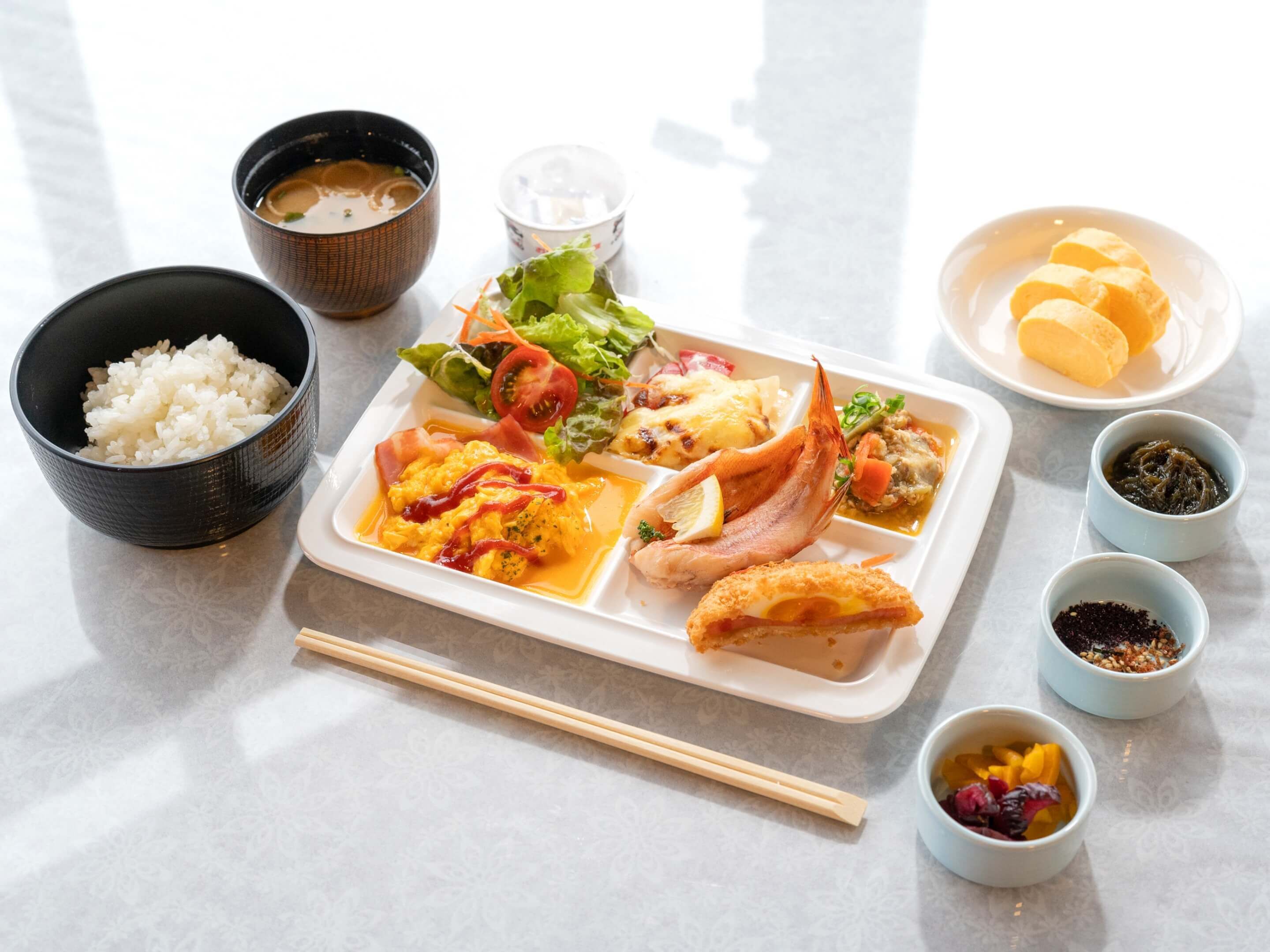 A meal tray with rice, scrambled eggs, ham, and vegetables.