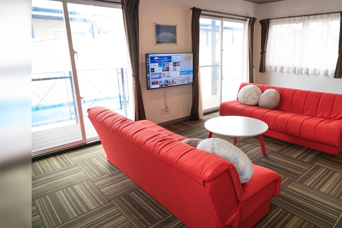 Une chambre d’hôtel avec un canapé rouge, une table ronde blanche et un téléviseur fixé au mur.