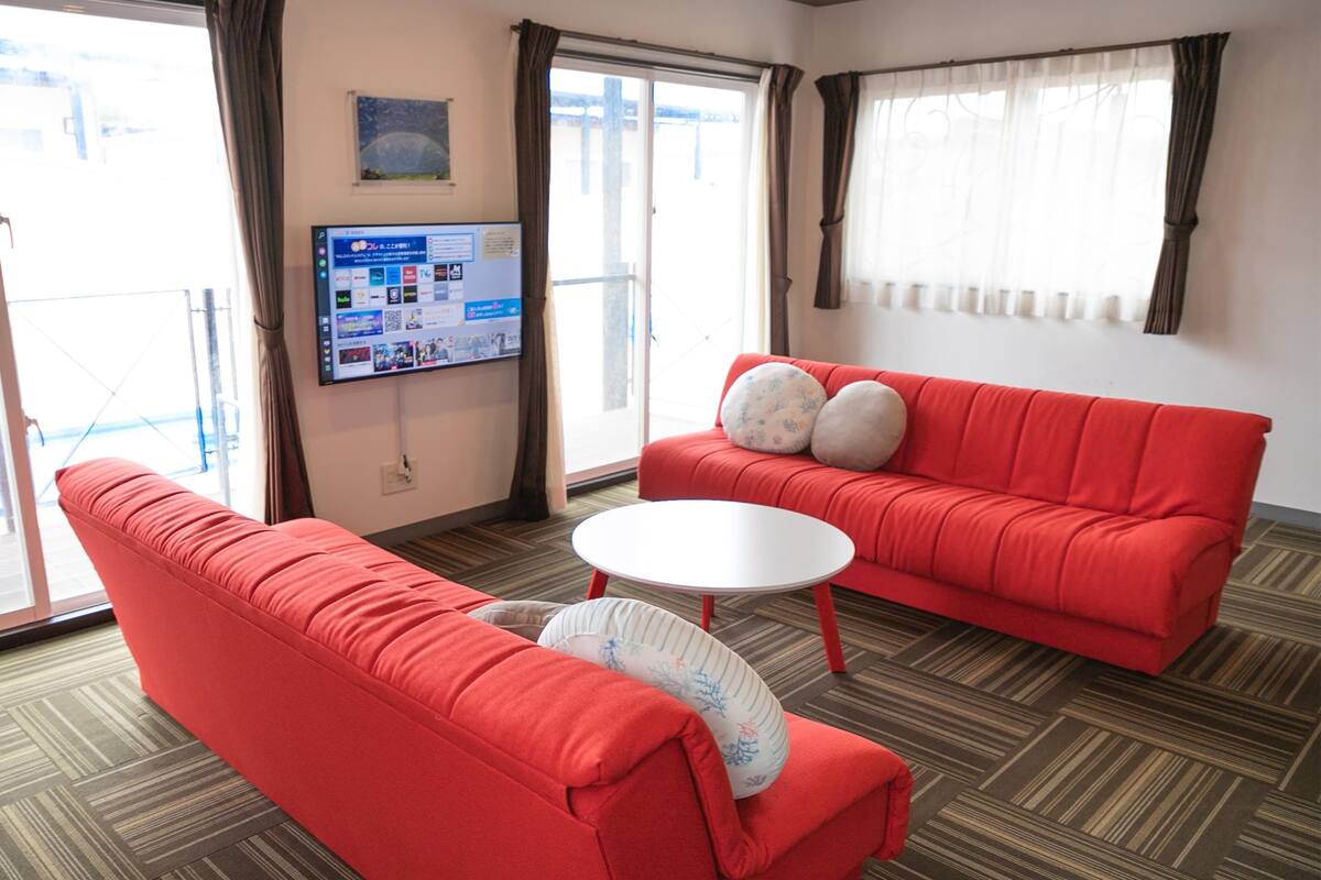 Une pièce avec un canapé rouge, une table basse blanche et un téléviseur fixé au mur.