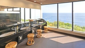 A bathroom with a black marble sink, two wicker stools, and a large window with a view of the ocean.