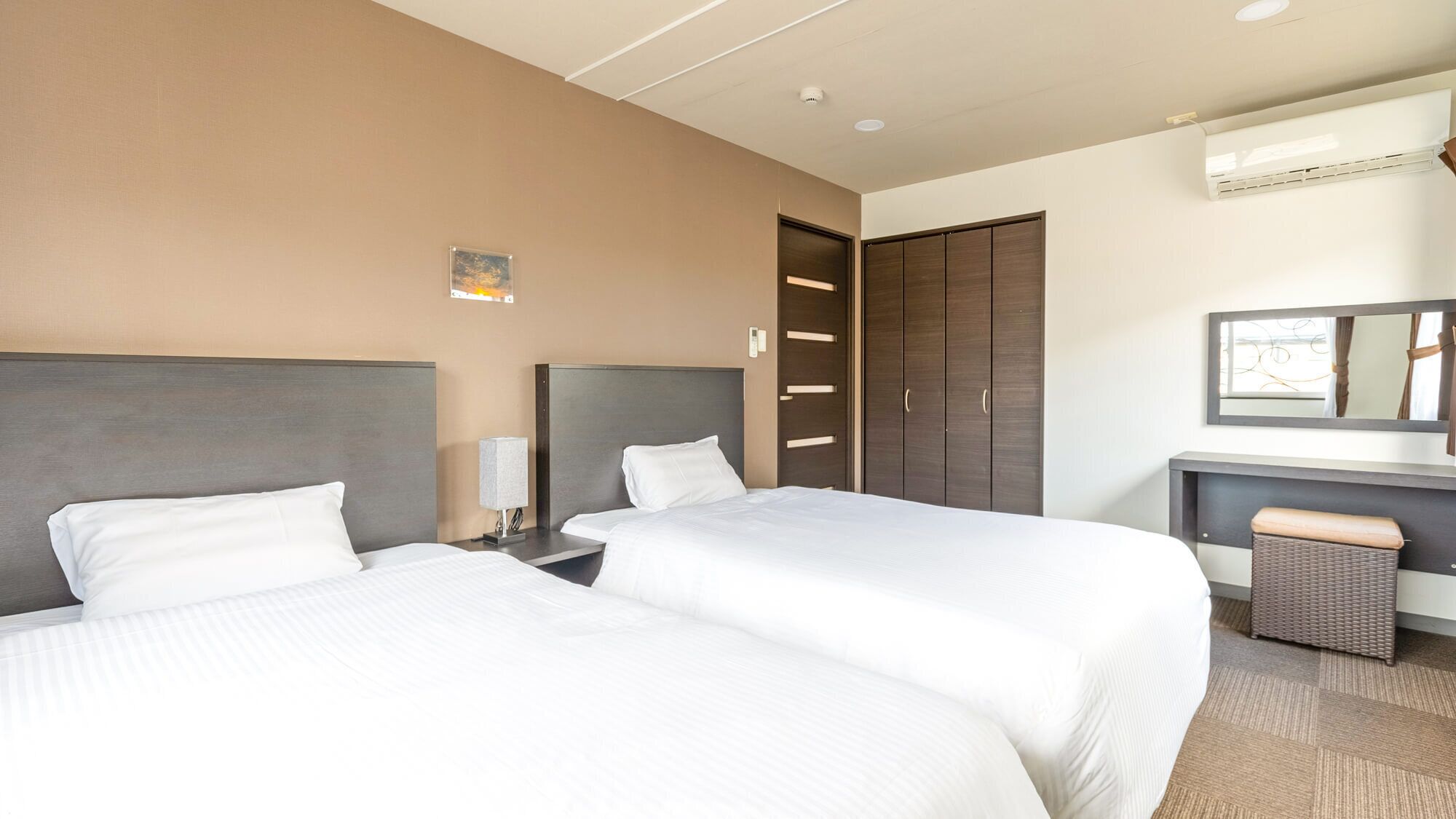 Een hotelkamer met twee bedden, een bureau met stoel, een garderobe en een spiegel.