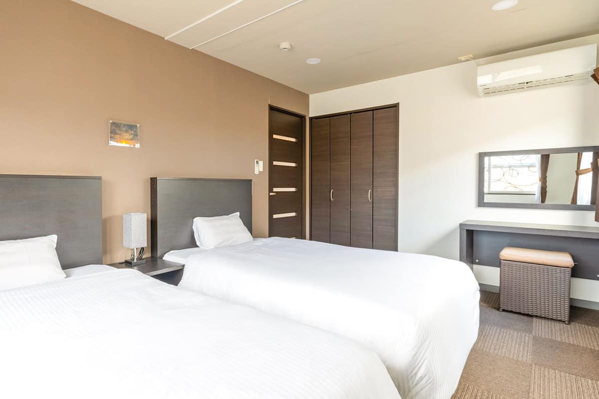 Une chambre d’hôtel avec deux lits, un bureau avec une chaise, une armoire et un miroir.