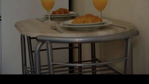 Une petite table ronde avec un cadre en métal, deux verres de jus d’orange, une assiette de croissants et une fourchette.