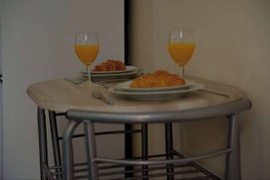 Ein kleiner runder Tisch mit Metallgestell, zwei Orangensaftgläser, ein Teller mit Croissants und eine Gabel.