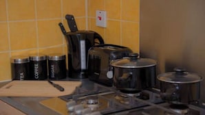 Une cuisine équipée d’une cuisinière, de casseroles, d’une machine à café et de récipients étiquetés pour le thé, le café et le sucre.