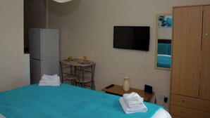 Une chambre d’hôtel comprenant un lit, un bureau, une chaise, une télévision, une armoire et une petite table avec un vase.