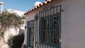 Un edificio con fachada blanca, puerta verde y una ventana con celosías metálicas decorativas.