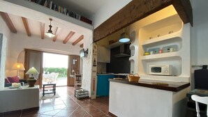 Amplia sala de estar con cocina, suelo de baldosas, vigas de madera y un balcón con mobiliario exterior.