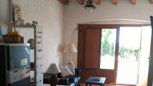 Una habitación con techo de madera, un ventilador de techo, una mesa con lámpara, un sofá y una puerta que da al exterior.