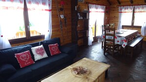 A cozy wooden cabin interior with a sofa, a wooden coffee table, and a dining area.