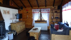 A cozy cabin interior with a stone floor, wooden furniture, a fireplace, and a television.