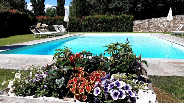 A swimming pool with lounge chairs and a flower bed in the foreground. - Three-room apartment, 80 square meters, 5/7 persons with swimming pool, 8 km from the center of Florence (Scandicci, Firenze)