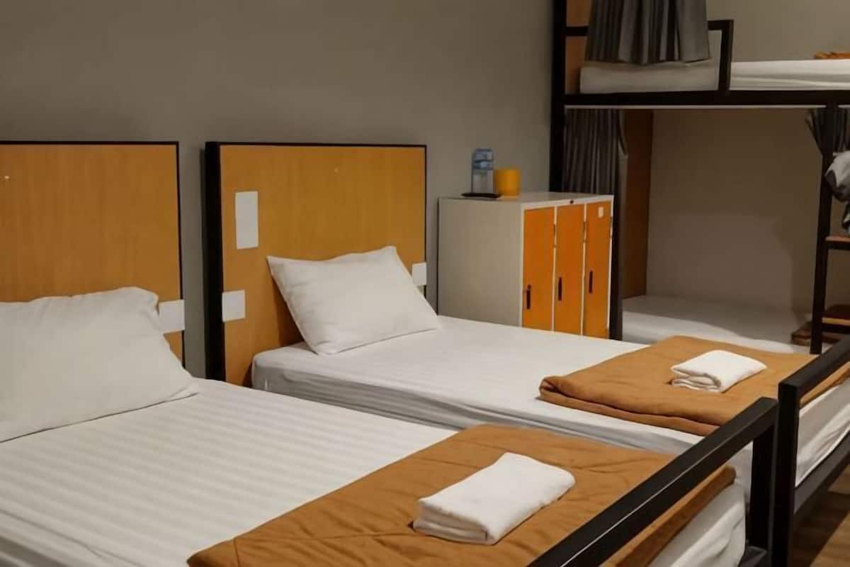Une chambre d’hôtel avec deux lits simples, un lit superposé, une armoire et une petite table avec une lampe.