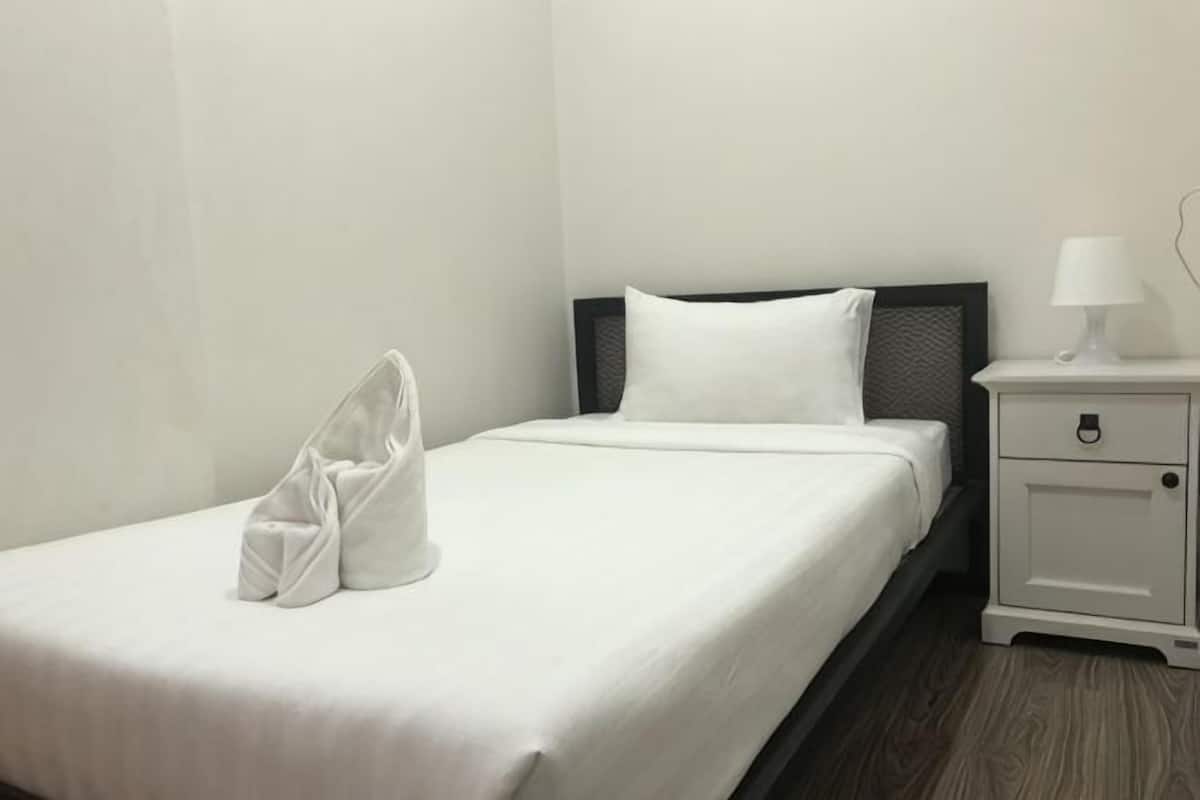 Un lit bien fait, avec une couette blanche et des oreillers, une petite table de chevet avec une lampe, et une paire de chaussures posées sur le lit.