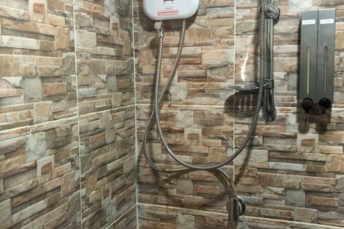 A shower area with a stone wall design, a handheld showerhead, and a wall-mounted control panel.