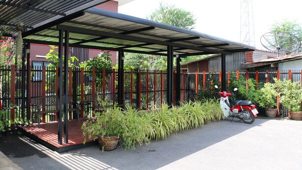 Un espace extérieur abrité, délimité par une clôture en métal, agrémenté de plantes en pot et où est garé un scooter.