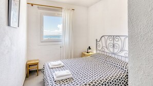 A bedroom with a bed, a nightstand, a window with curtains, and a view of the sky. - Golden Sunset Views - Panoramic Ocean View Duplex (Roses)