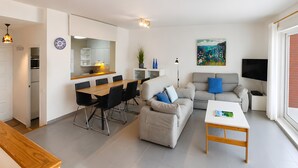 A modern apartment with a dining area, sofa, TV, and a painting. - Golden Sunset Views - Panoramic Ocean View Duplex (Roses)