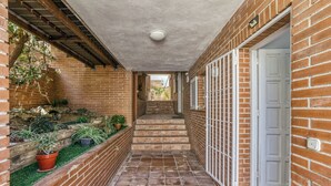 A narrow brick corridor with a tiled floor, a white door on the right, and potted plants along the left wall. - Golden Sunset Views - Panoramic Ocean View Duplex (Roses)