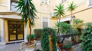 A courtyard with a stone wall, potted plants, and a statue of an angel. - Rome Boutique Apartments, central, delightful, close to the center and the vatican (6900333)