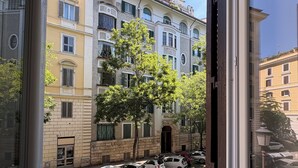 A view from a window of a multi-story building with parked cars and a tree in the foreground. - Rome Boutique Apartments, central, delightful, close to the center and the vatican (6900333)