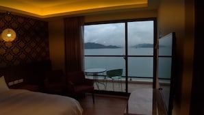 A hotel room with a large window offering a view of a body of water and distant land. There is a bed, two chairs, and a small table. - Miracolo View Hotel (Yuchi)