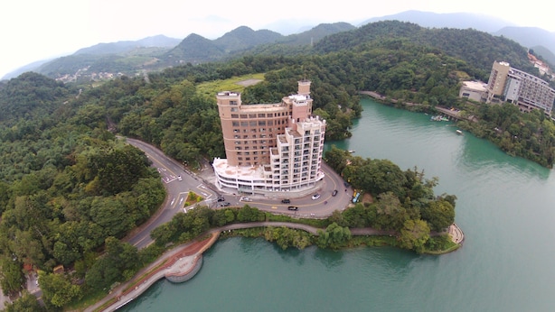 An aerial view of a multi-story hotel with a central courtyard, surrounded by lush greenery and a body of water. - Miracolo View Hotel (Yuchi)